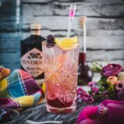 Refreshing blackberry raspberry gin fizz, garnished with a lemon wedge and a blackberry, placed on marbled plate.