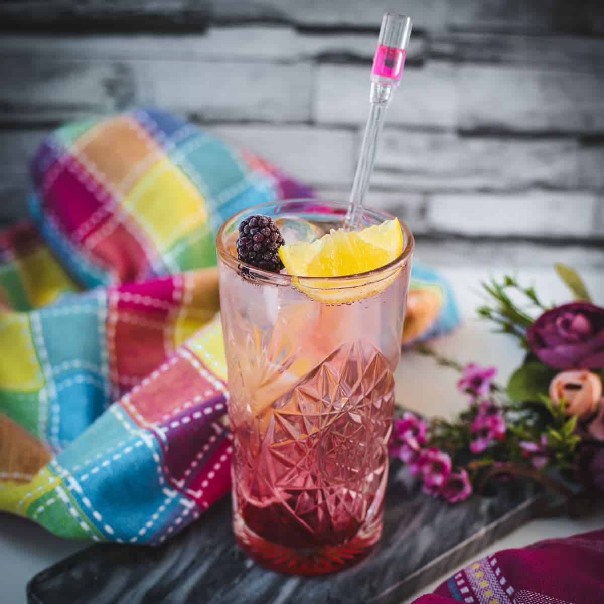 Refreshing blackberry raspberry gin fizz, garnished with a lemon wedge and a blackberry, placed on marbled plate.