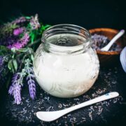 Gorgeous preserving glass, filled with homemade lavender coffee creamer. Placed on dark ground covered with dried lavender buds.