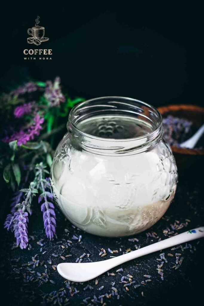 Gorgeous preserving glass, filled with homemade lavender coffee creamer. Placed on dark ground covered with dried lavender buds.