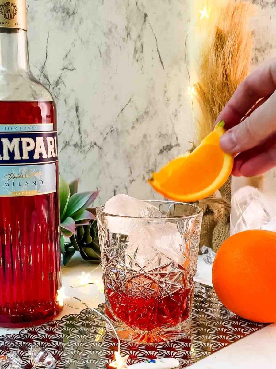 Hand placing orange wedge on top of the Negroni cocktail.