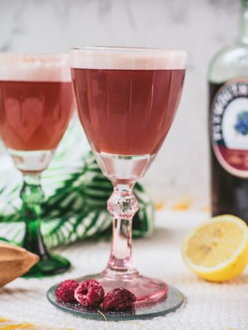 Divine ruby fizz cocktail, placed on mirrored coaster and served in a red and a green glass.
