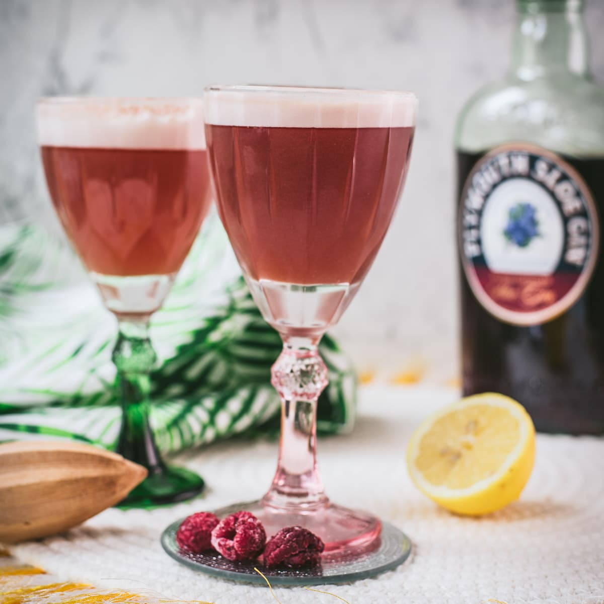 Divine ruby fizz cocktail, placed on mirrored coaster and served in a red and a green glass.