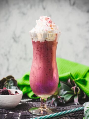 Boozy berry adult milkshake with homemade Chambord, served in Hurricane glass. Garnished with whipped cream and dusted with edible glitter. Served with a drinking straw.