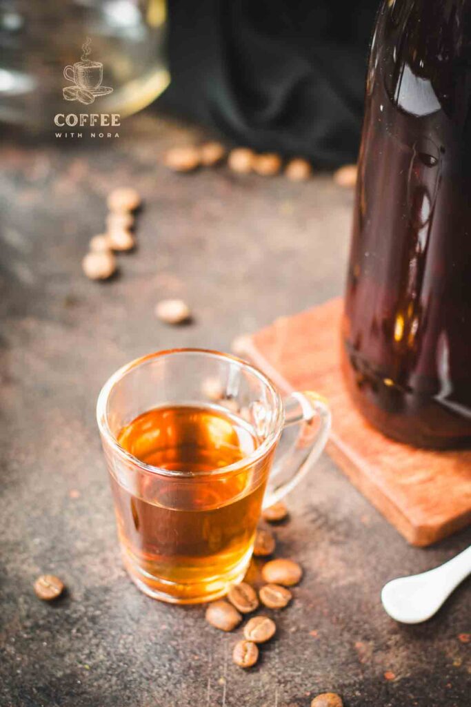 Amazing coffee syrup, in small glass, placed on brown ground next to coffee beans.