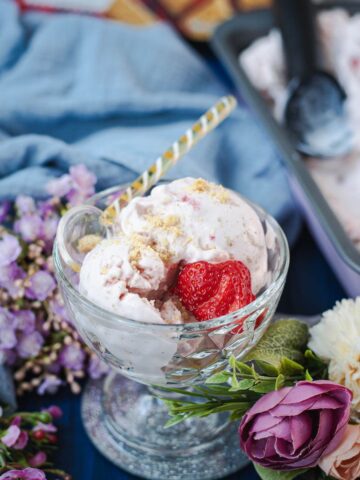 Glass serving bowl, filled with delicious strawberry shortcake ice cream. Garnished with fresh strawberries and shortbread cookie crumbs.