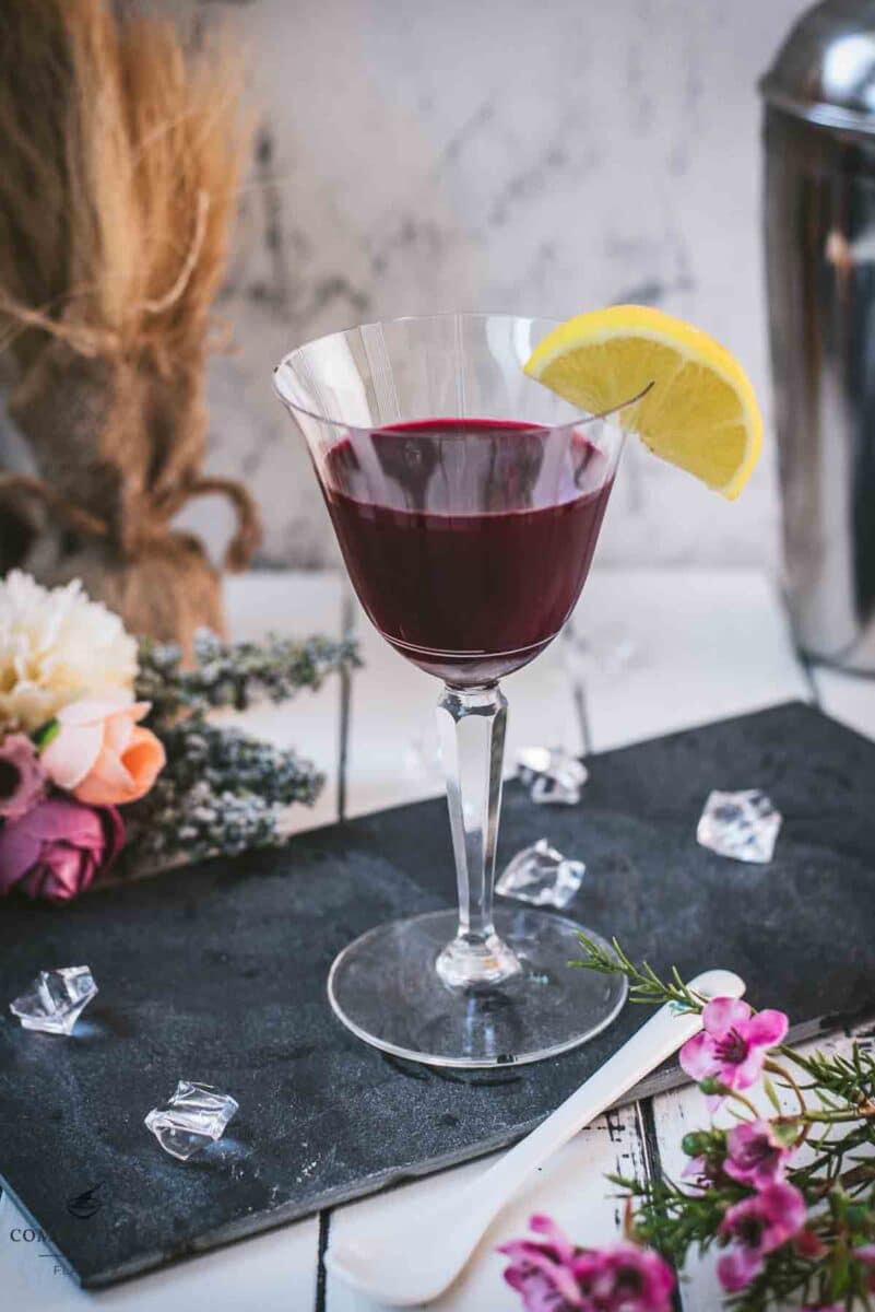 Elegant, dark red beetroot sour, garnished with a lemon wedge. Placed on a black slate plate.