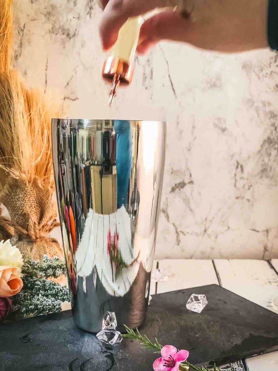 Add orange bitters to the cocktail shaker.