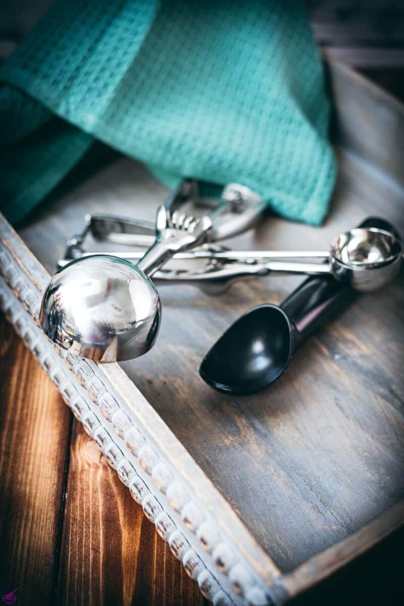 Three different cookie scoops displayed on a wooden tray.