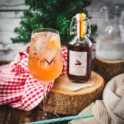 Delicious Zirben Spritzer served in white wine glass. Placed on wooden ground, next to a flask of Zirben Schnapps.