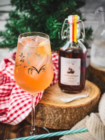 Delicious Zirben Spritzer served in white wine glass. Placed on wooden ground, next to a flask of Zirben Schnapps.