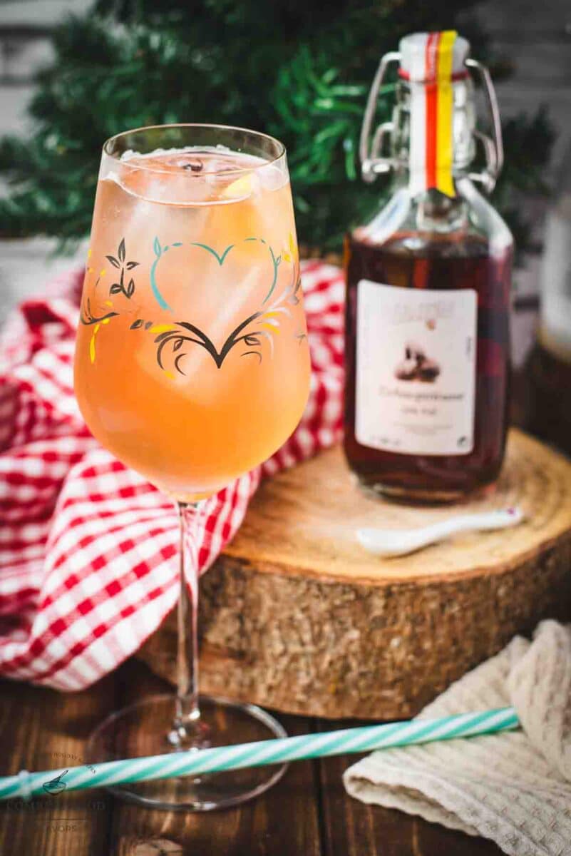 Delicious Zirben Spritzer served in white wine glass. Placed on wooden ground, next to a flask of Zirben Schnapps.