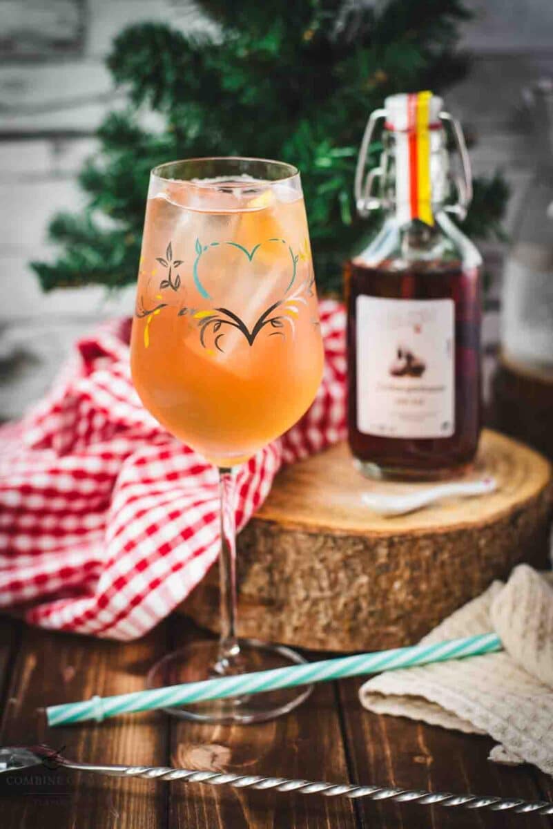 Delicious Zirben Spritzer served in white wine glass. Placed on wooden ground, next to a flask of Zirben Schnapps.