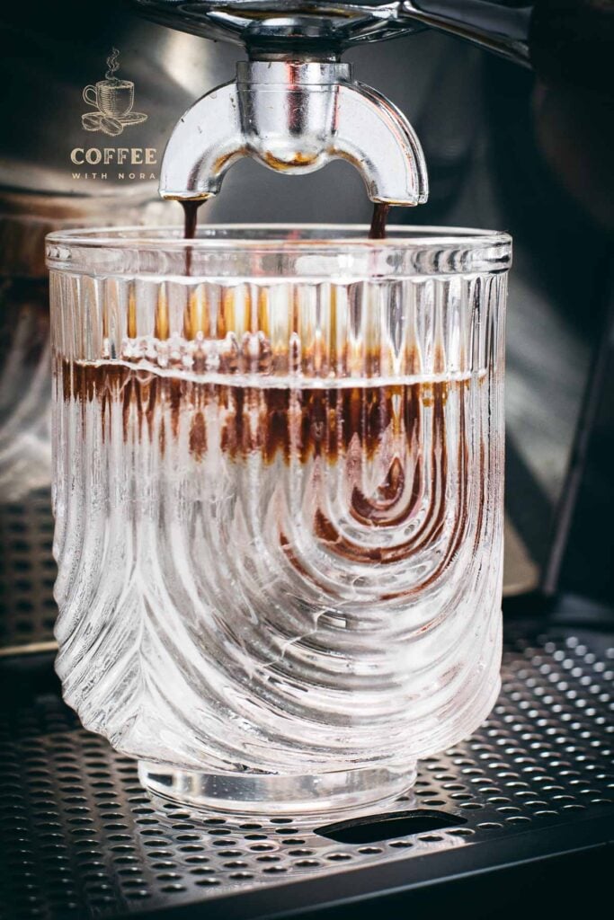 Brewing process of iced Americano into a iced and cold water filled serving glass, using an espresso machine.