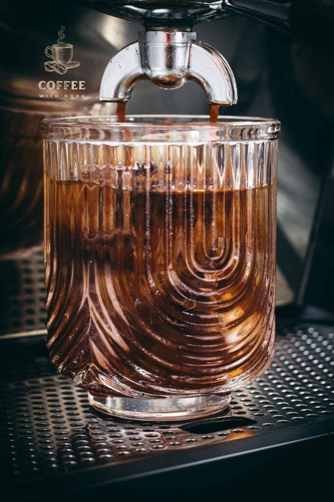 Brewing process of iced Americano into a iced and cold water filled serving glass, using an espresso machine.