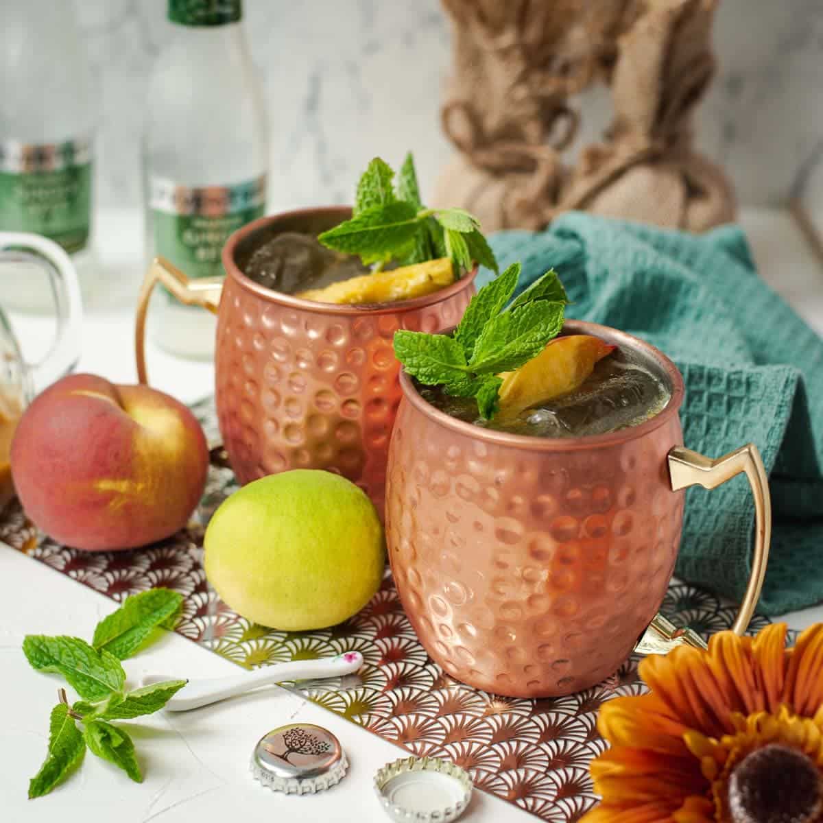 Delicious peach Moscow mule, served in copper mugs, garnished with peach slices and mint.