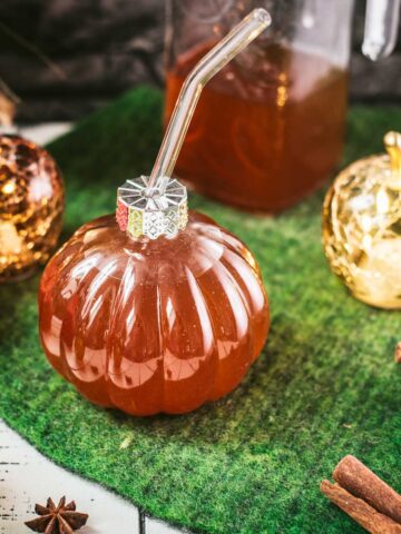 Homemade spiced apple cider in pumpkin shaped drinking glass.