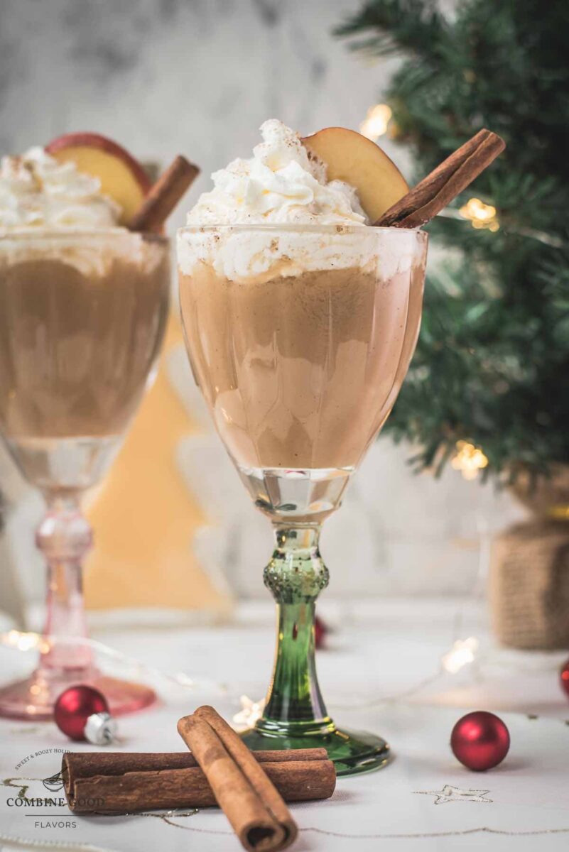 Decadent apple cider eggnog, garnished with a cinnamon stick, whipped cream, and apple slices.