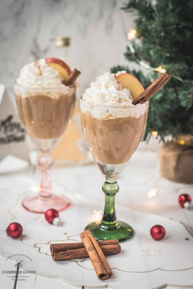 Decadent apple cider eggnog, garnished with a cinnamon stick, whipped cream, and apple slices.
