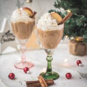 Decadent apple cider eggnog, garnished with a cinnamon stick, whipped cream, and apple slices.