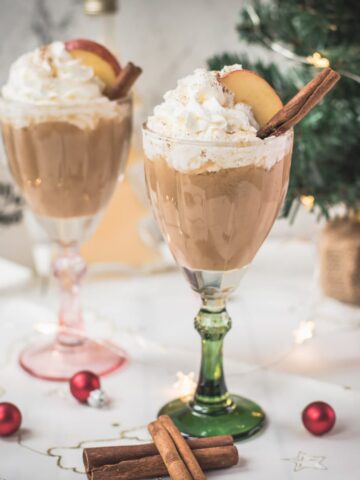 Decadent apple cider eggnog, garnished with a cinnamon stick, whipped cream, and apple slices.