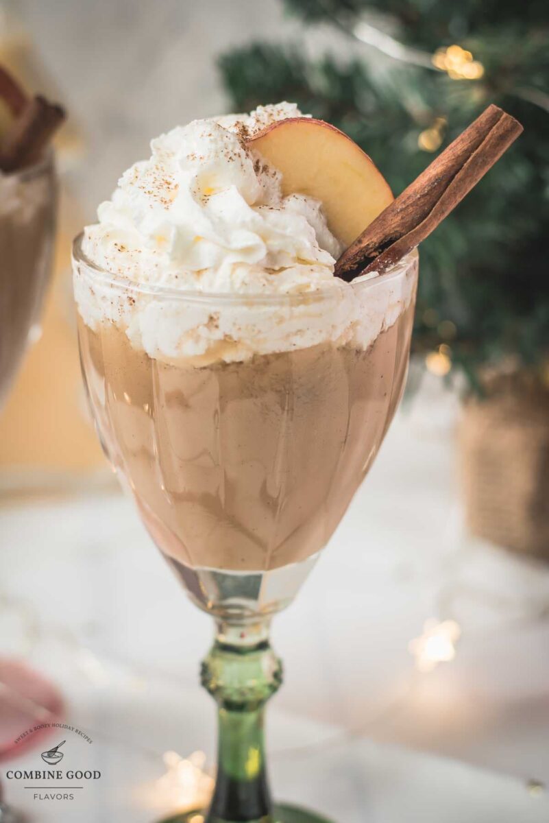 Decadent apple cider eggnog, garnished with a cinnamon stick, whipped cream, and apple slices.
