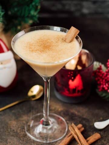 Delicious eggnog martini dusted with ground cinnamon and garnished with a cinnamon stick.