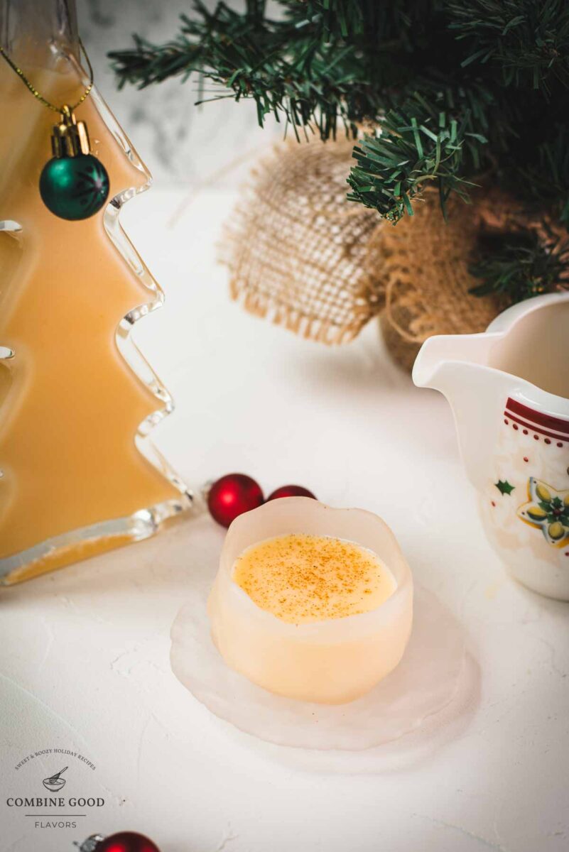 Delicious eggnog in a small icy bowl next to a Christmas tree shaped bottle, filled with eggnog.