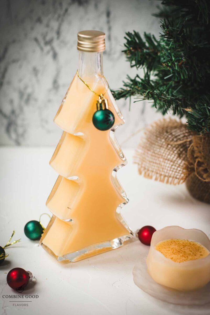 Delicious eggnog in a small icy bowl next to a Christmas tree shaped bottle, filled with eggnog.