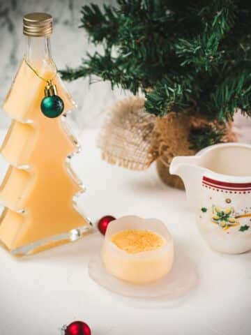 Delicious eggnog in a small icy bowl next to a Christmas tree shaped bottle, filled with eggnog.