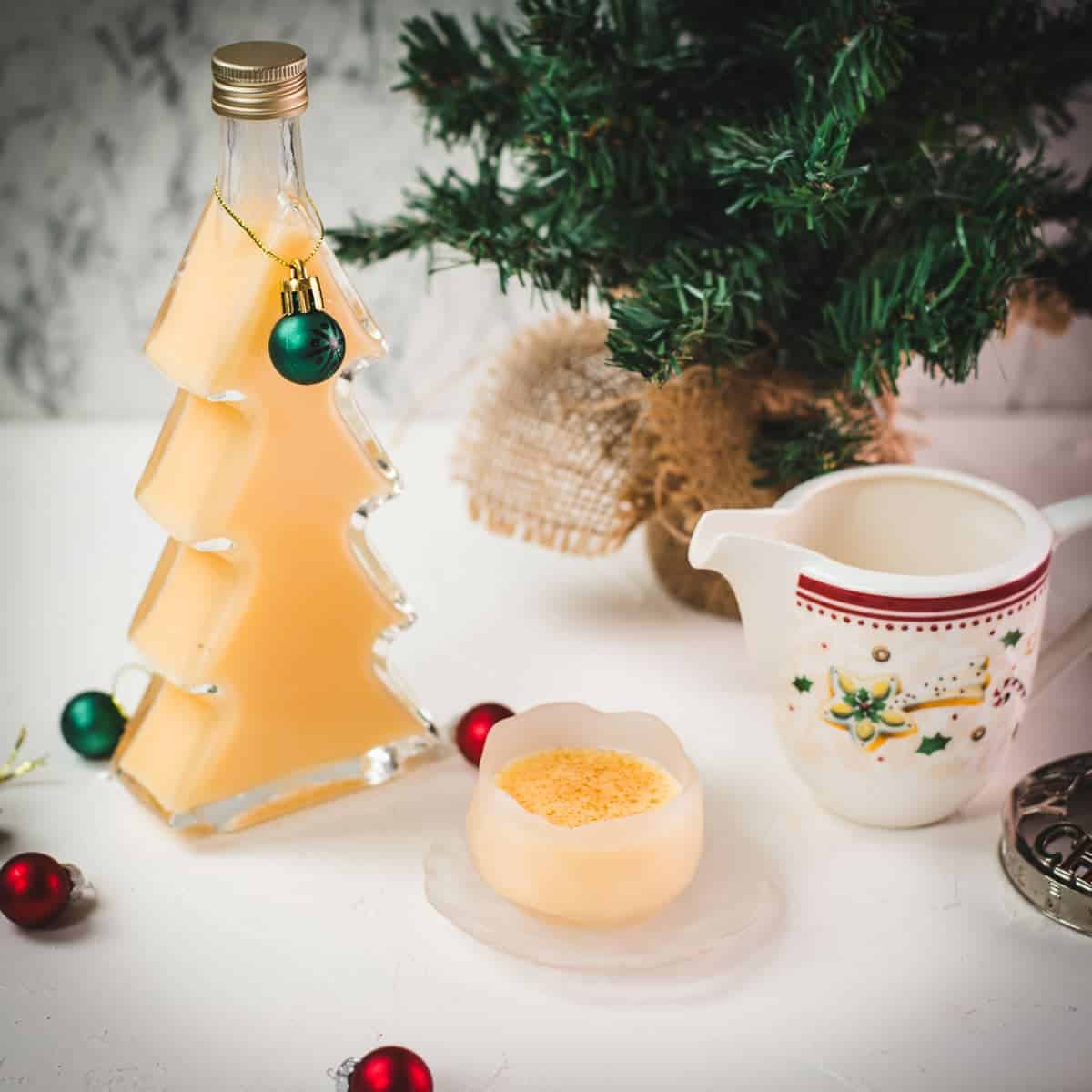 Delicious eggnog in a small icy bowl next to a Christmas tree shaped bottle, filled with eggnog.