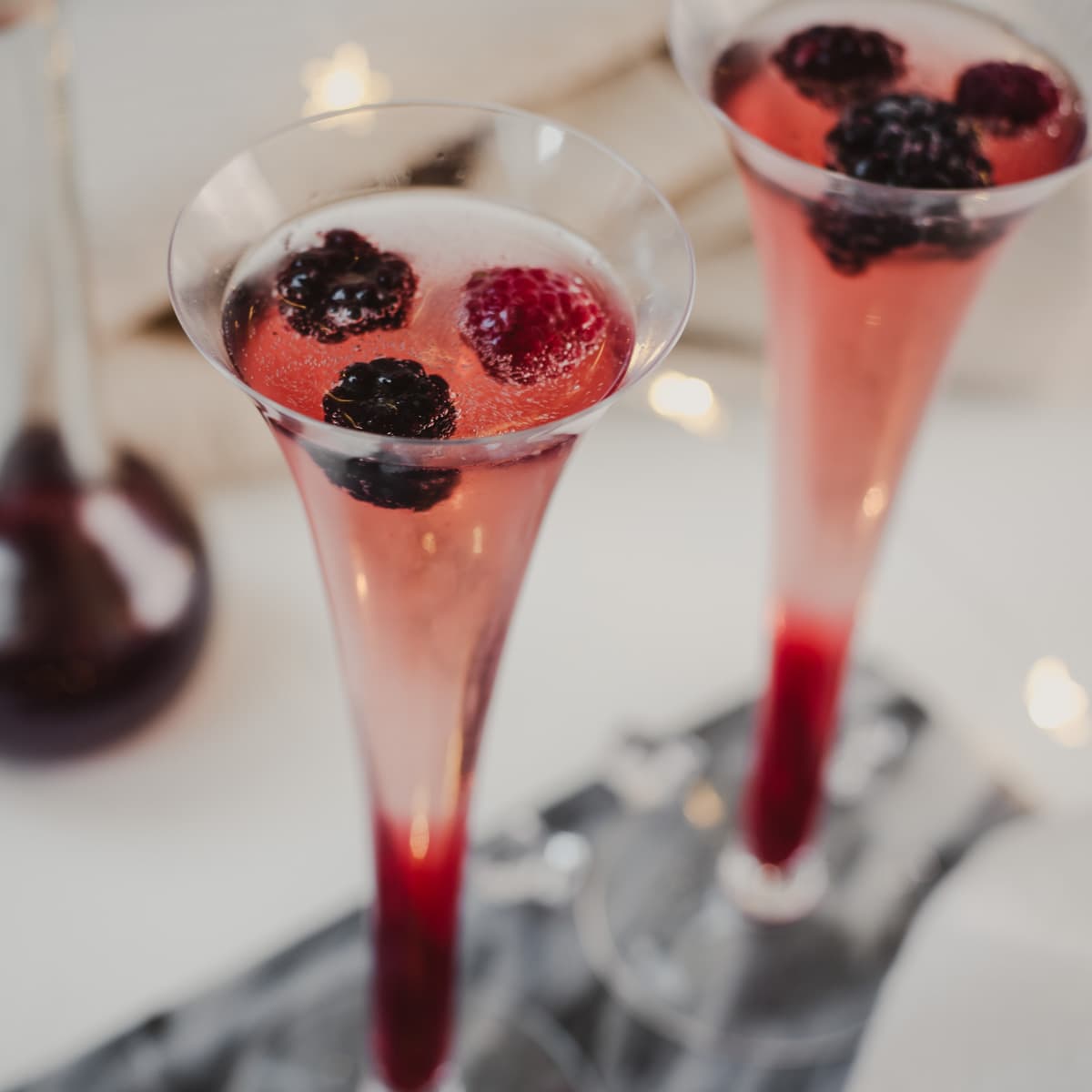Sparkling wine and chambord cocktail served in two champagne flutes. Garnished with berries.