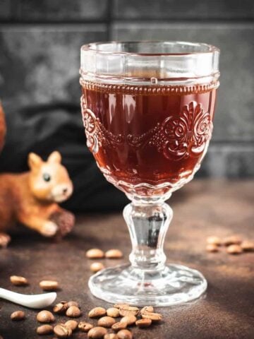 Gorgeous glass filled with maple syrup coffee, placed on dark brown ground, next to squirrel figure.