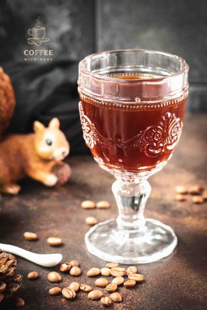 Gorgeous glass filled with maple syrup coffee, placed on dark brown ground, next to squirrel figure.