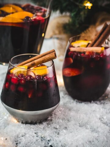 Gorgeous glasses filled with delicious winter sangria, garnished with a cinnamon stick. Placed on snow covered ground.