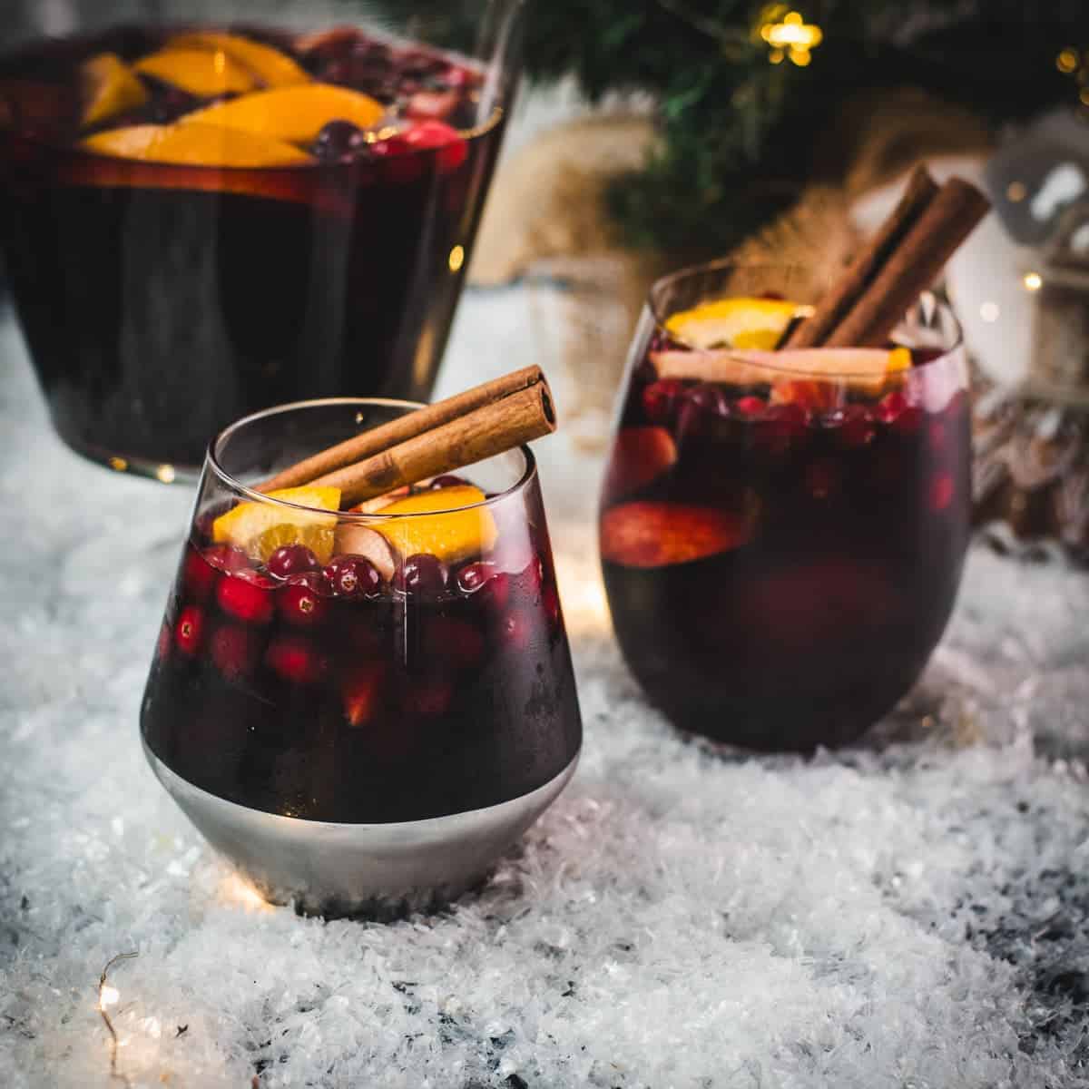 Gorgeous glasses filled with delicious winter sangria, garnished with a cinnamon stick. Placed on snow covered ground.