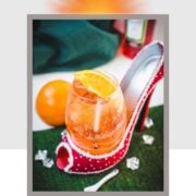 Aperol spritz with white wine instead of prosecco playfully served in a red and white polka dot high heel. Garnished with n orange slice.
