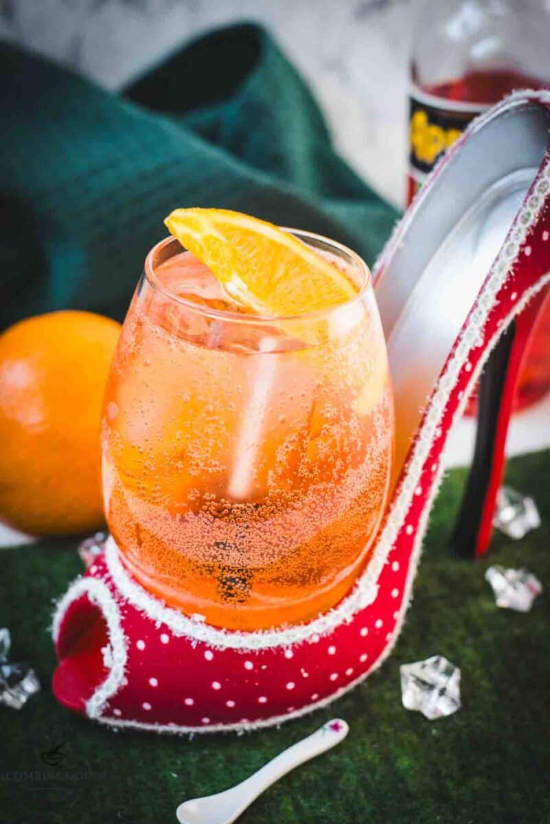 Aperol spritz with white wine instead of prosecco playfully served in a red and white polka dot high heel. Garnished with n orange slice.