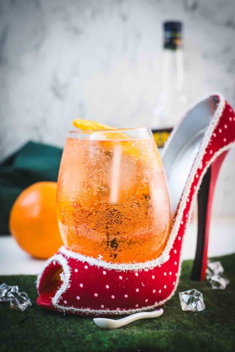 Aperol spritz with white wine instead of prosecco playfully served in a red and white polka dot high heel. Garnished with n orange slice.
