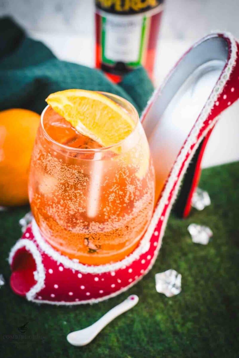 Aperol spritz with white wine instead of prosecco playfully served in a red and white polka dot high heel. Garnished with n orange slice.