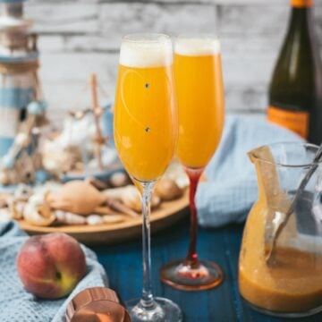 Beautiful champagne flutes, filled with delicious peach Bellini. Placed on blue, wooden ground.