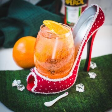 Aperol spritz with white wine instead of prosecco playfully served in a red and white polka dot high heel. Garnished with n orange slice.