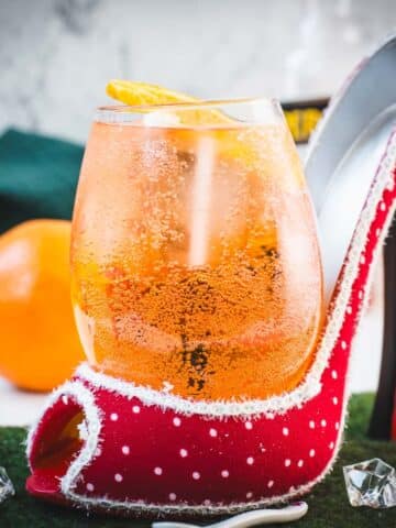 Aperol spritz with white wine instead of prosecco playfully served in a red and white polka dot high heel. Garnished with n orange slice.