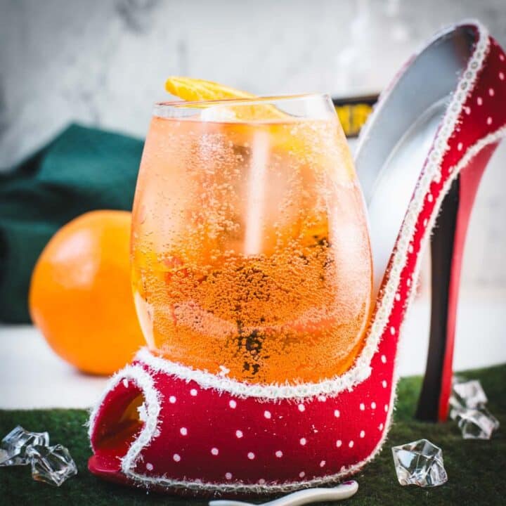 Aperol spritz with white wine instead of prosecco playfully served in a red and white polka dot high heel. Garnished with n orange slice.