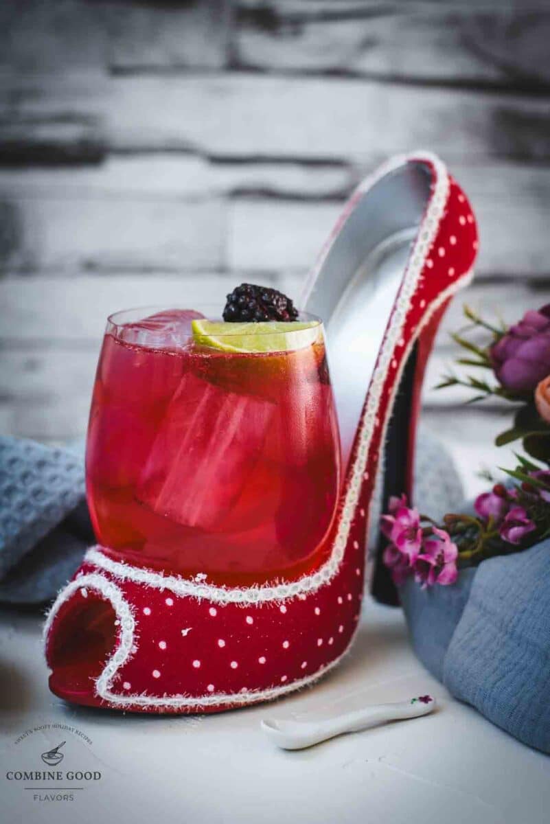 Chambord gin and tonic playfully placed in a red and white polka dot high heel. Garnished with a lime wedge and a black berry.