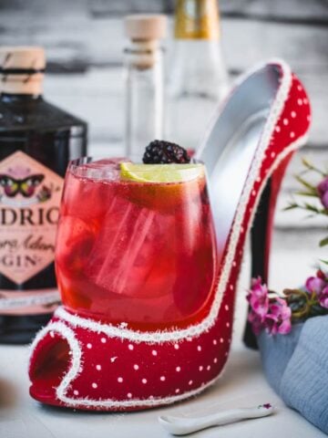 Chambord gin and tonic playfully placed in a red and white polka dot high heel. Garnished with a lime wedge and a black berry.
