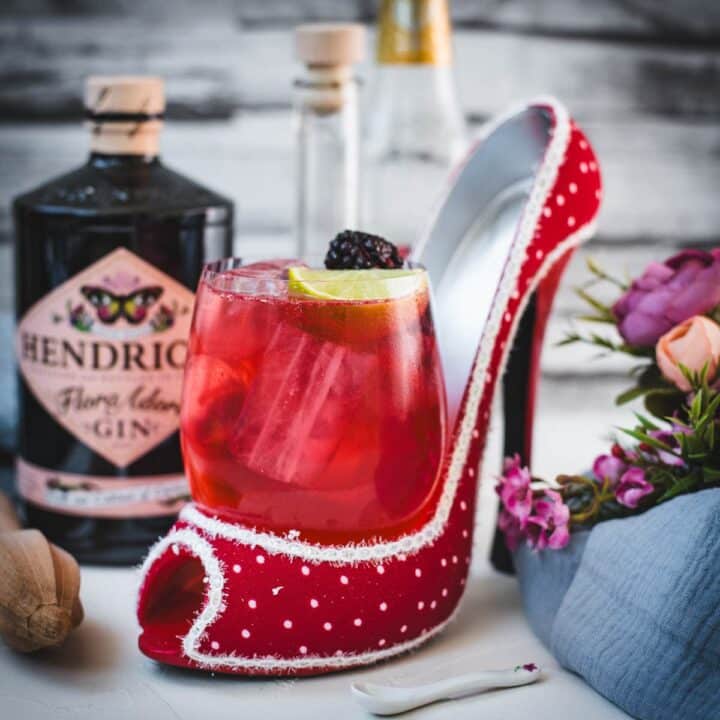 Chambord gin and tonic playfully placed in a red and white polka dot high heel. Garnished with a lime wedge and a black berry.