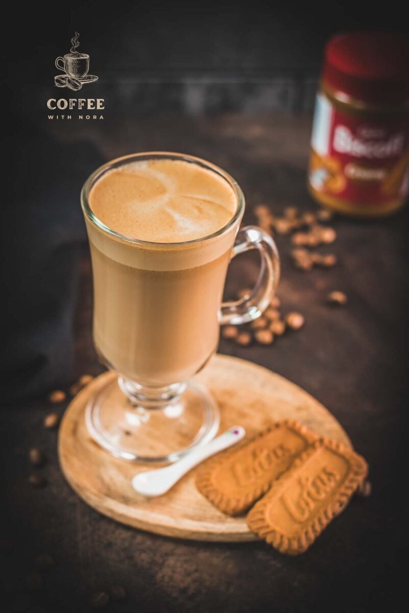 Super quick Biscoff Latte placed on small wooden plate next to two Biscoff cookies.