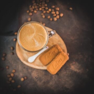 Super quick Biscoff Latte placed on small wooden plate next to two Biscoff cookies.