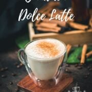 Glass mug filled with delicious cinnamon dolce latte, dusted with cinnamon, and placed on wooden coaster.